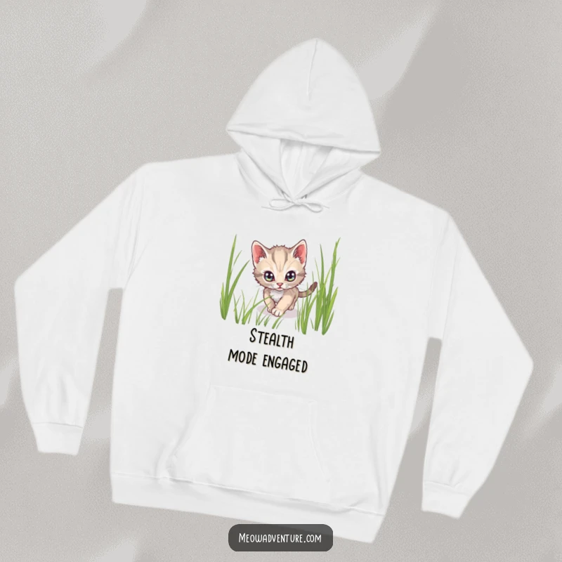 Funny hoodie showing a stealthy kitten with wide, alert eyes tiptoeing through tall grass, ideal for cozy spying.